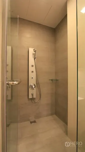 Condominium for rent in Khlong Toei, Bangkok - Walk-in shower with glass door and multi-function shower panel in neutral tiles.