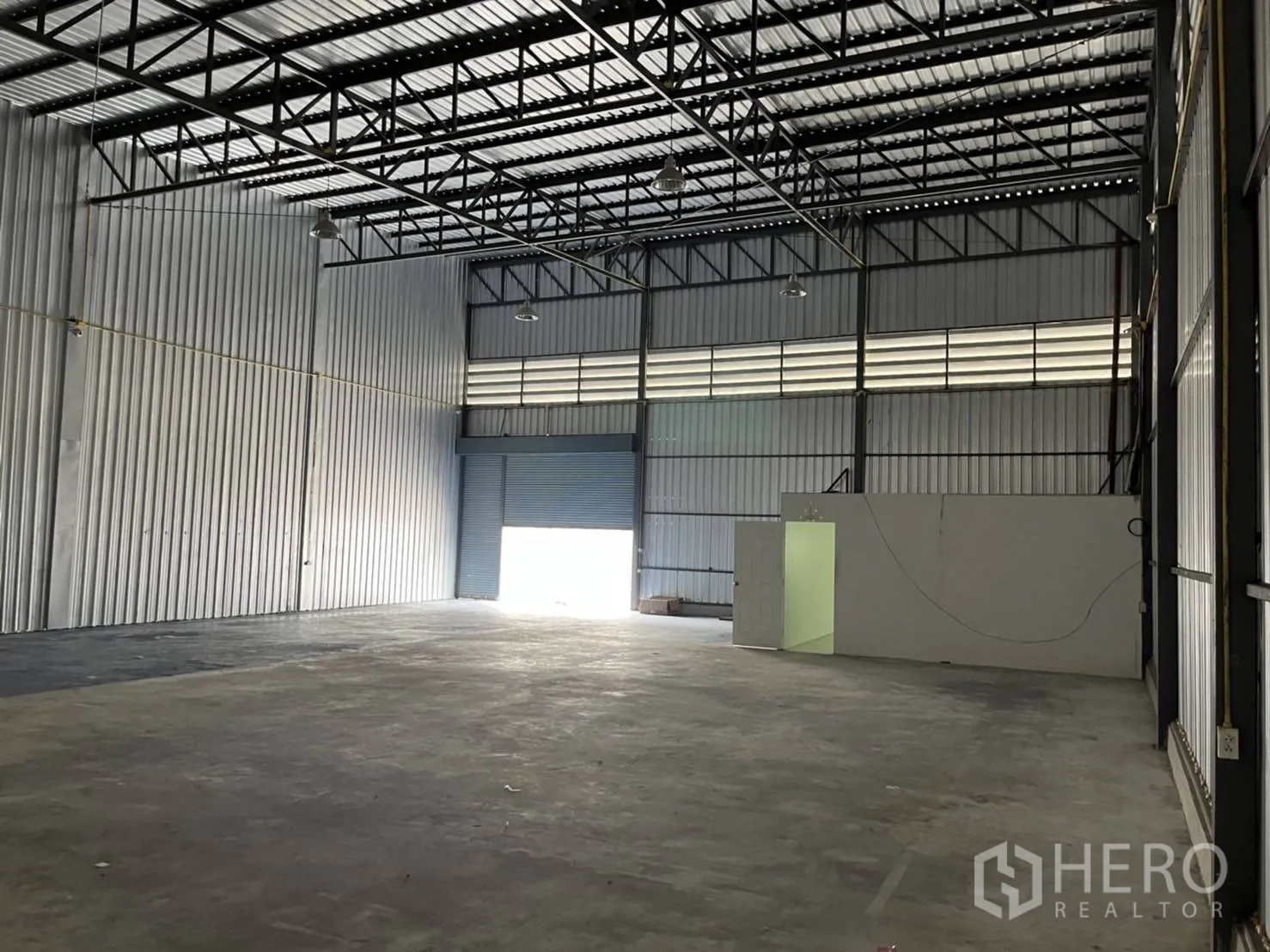 Warehouse for rent in Bang Phli, Samut Prakan - Interior angle showing high roof structure, roller shutter, and office partition.