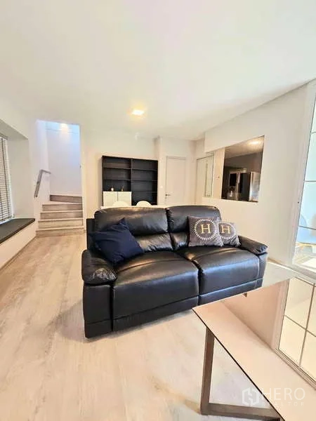 Detached House for rent or sale in Prawet, Bangkok - Living room with black leather sofa facing shelving and the stairwell beyond.