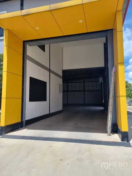Warehouse for rent or sale in Krathum Baen, Samut Sakhon - Covered high-clearance loading bay with bold yellow cladding and wide driveway for trucks.