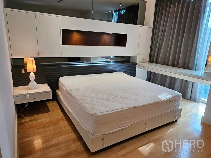 Condominium for rent or sale in Pathum Wan, Bangkok - Master bedroom with wood flooring, built-in cabinetry and large windows with blackout curtains.