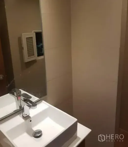 Apartment for rent in Khlong Toei, Bangkok - Contemporary bathroom with square basin, large wall mirror, and neutral tiled walls.