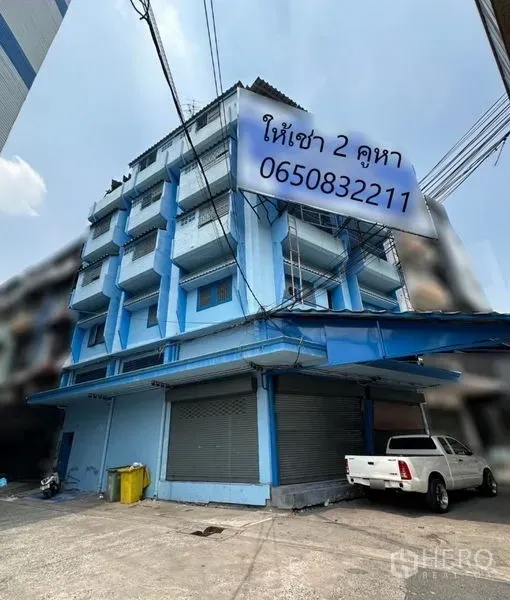 店屋 出租在Bang Na, Bangkok - 蓝色外立面的转角五层店屋，带阳台和金属卷闸门，位于Bang Na。