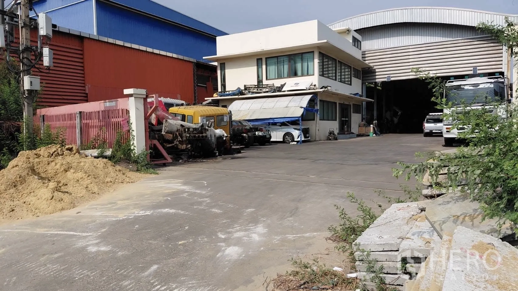 Warehouse for rent in Bang Phli, Samut Prakan - Front approach to warehouse compound with wide driveway, boundary wall, and parking for heavy vehicles.