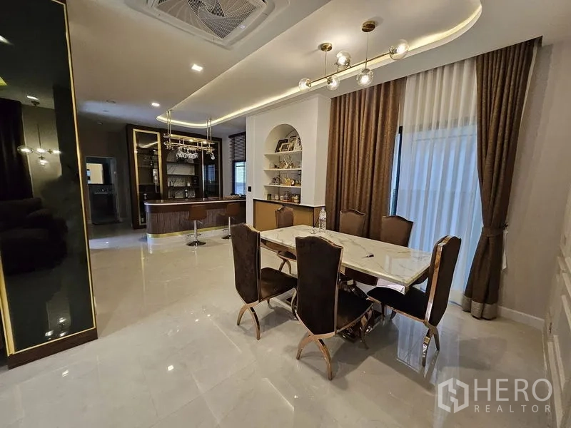 Detached House for sale in Mueang Pathum Thani, Pathum Thani - Open-plan dining room with marble table, gold-accent lighting and built-in bar shelving.