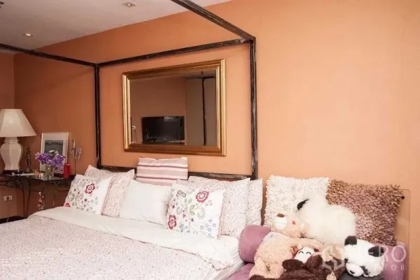 Condominium for rent in Watthana, Bangkok - Cozy bedroom with canopy-style bed, floral pillows, gold-framed mirror and warm peach walls.