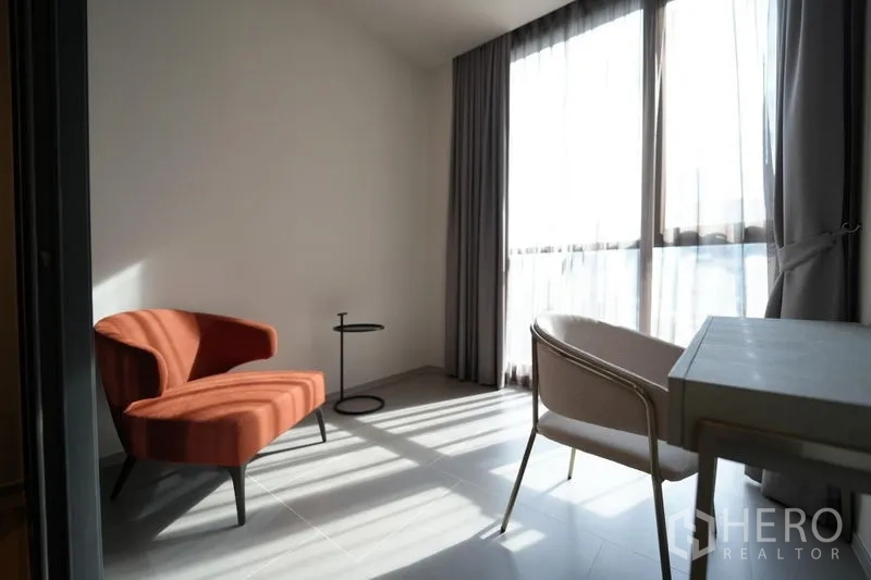 Condominium for rent - Sunlit multipurpose room with orange lounge chair, side table and work desk by wide windows.