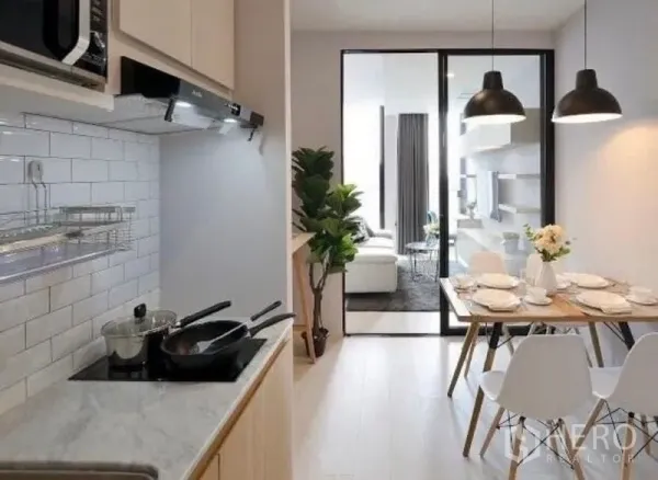 คอนโด ให้เช่าในPathum Wan, Bangkok - ครัวรูปตัวไอพร้อมผนังกระเบื้องสีขาว เตาไฟฟ้า และโต๊ะทานอาหารใต้โคมไฟแขวน