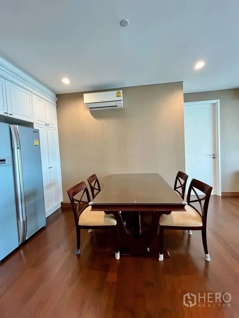 Condominium for rent in Watthana, Bangkok - Dining area with four chairs beside a double-door fridge and white built-in cupboards.