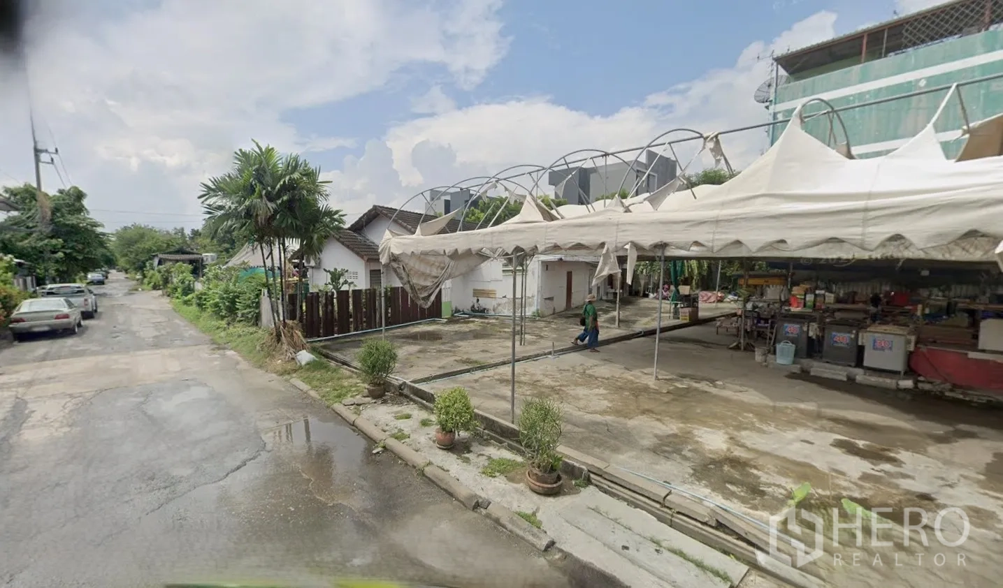 Land for rent in Bang Kapi, Bangkok - Street-side view of a paved corner lot with canopy frames and nearby low-rise houses.
