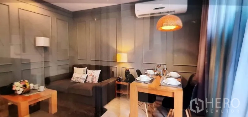 Condominium for rent in Phra Khanong, Bangkok - Open‑plan living room with paneled walls and four‑seat dining set.