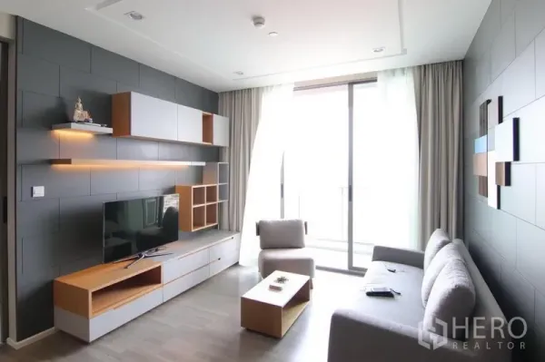 Condominium for rent in Bang Sue, Bangkok - Modern living room with L-shaped sofa, custom TV wall, and floor-to-ceiling sliding doors to the balcony.