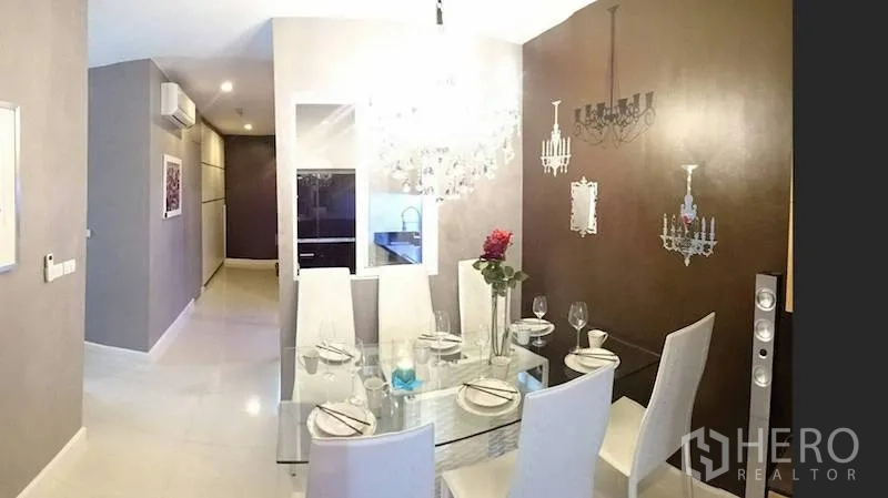 Condominium for rent or sale in Watthana, Bangkok - Dining area with glass table, six white chairs and a decorative chandelier feature wall.