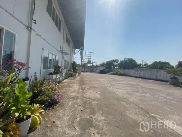 Factory for rent in Khlong Toei, Bangkok - Factory exterior yard with concrete driveway, planters and boundary wall on a sunny day.