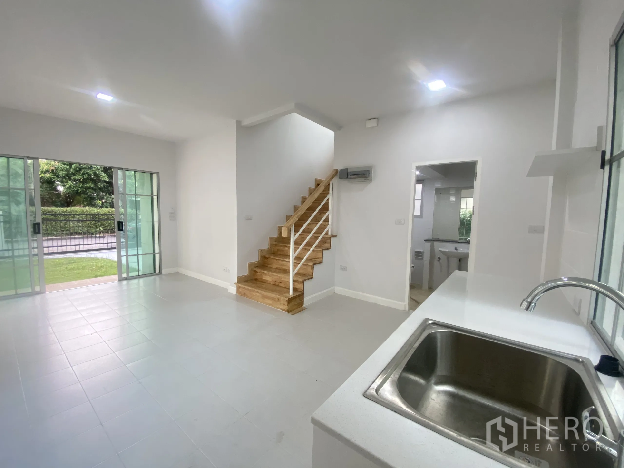 Detached House for sale in Nonthaburi - Bright open-plan living area with sliding glass doors, wood staircase and a kitchen sink.