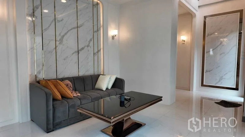 บ้าน ให้เช่าหรือขายในBang Na, Bangkok - มุมนั่งเล่นหรู ผนังลายหินอ่อน โซฟาสีเทา และพื้นกระเบื้องเงางาม