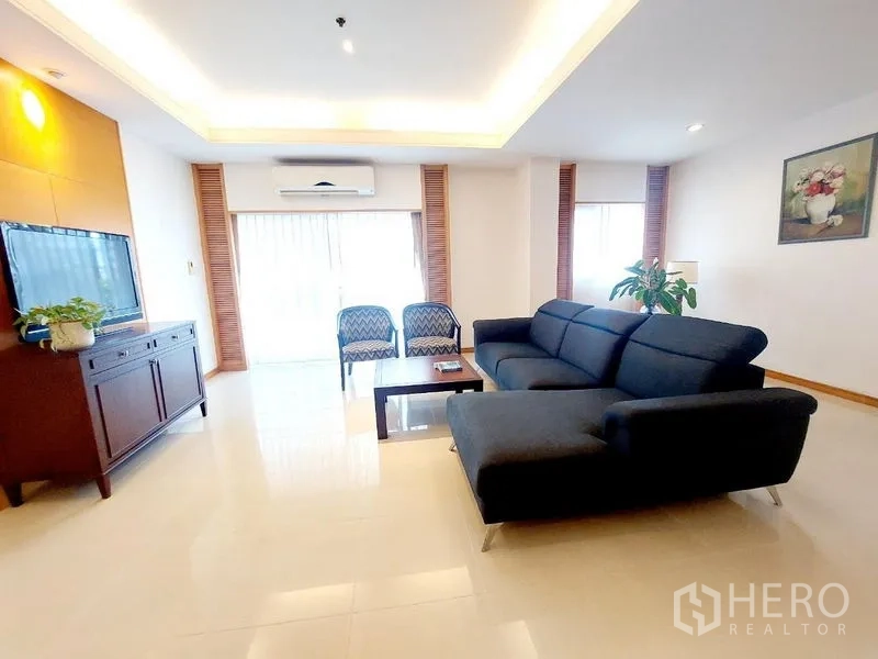 อพาร์ทเมนท์ ให้เช่า - มุมนั่งเล่นโปร่ง โซฟาแอล ตู้วางทีวี เก้าอี้คู่ และหน้าต่างบานใหญ่พร้อมมู่ลี่