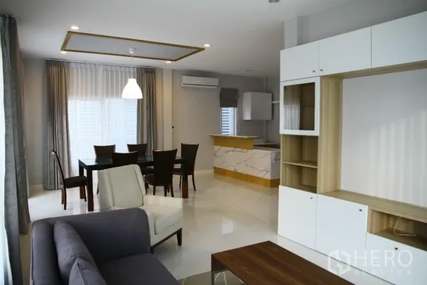 Detached House for rent or sale in Bang Na, Bangkok - Open-plan living and dining area with sofa set, dining table, built-in cabinet and marble breakfast bar by large windows.