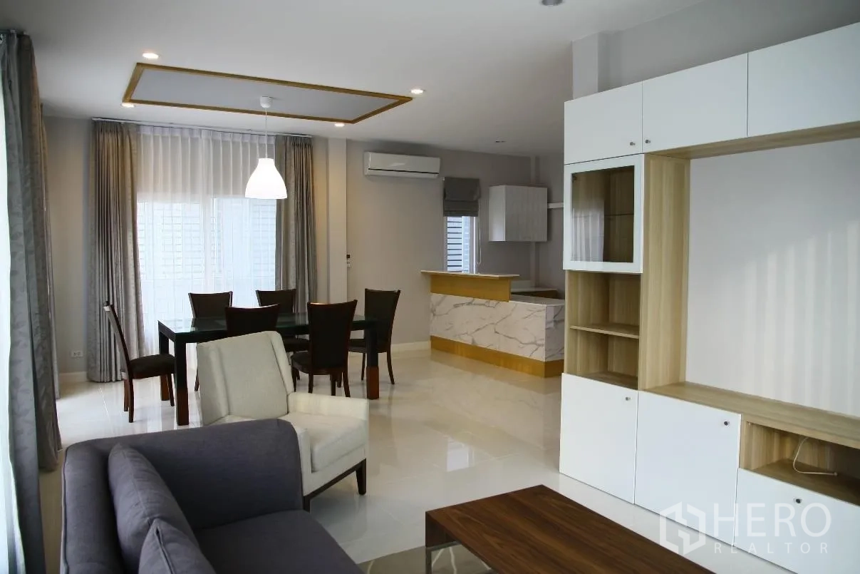 Detached House for rent or sale in Bang Na, Bangkok - Open-plan living and dining area with sofa set, dining table, built-in cabinet and marble breakfast bar by large windows.