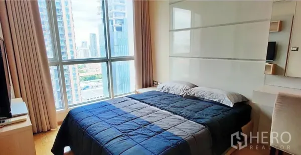 Condominium for rent in Ratchathewi, Bangkok - Cozy bedroom with large window and city view, double bed and neutral decor.
