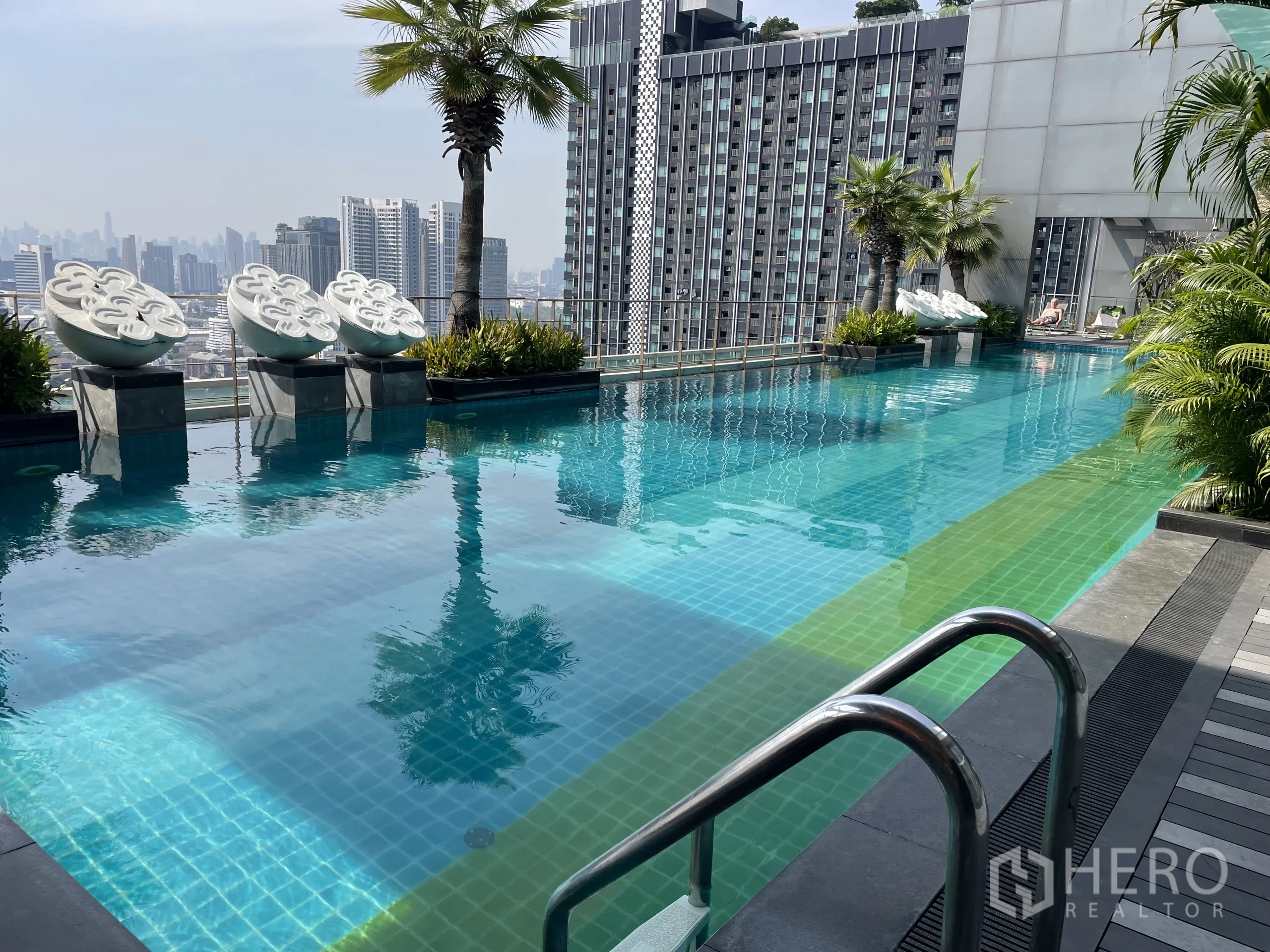 Condominium for sale in Chatuchak, Bangkok - Rooftop infinity pool with palm trees and a panoramic Bangkok skyline.