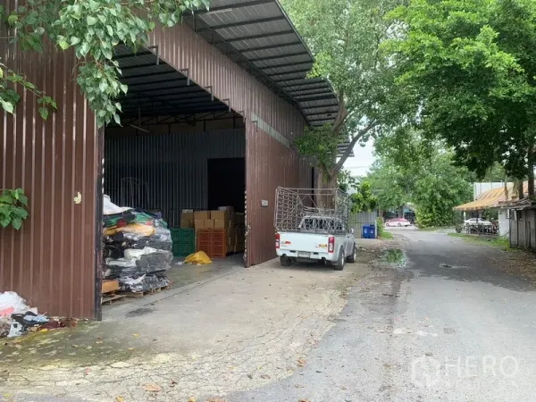 Warehouse for rent in Bang Kapi, Bangkok - Steel-clad warehouse with wide sliding doors, loading apron and pickup on a tree-lined lane in Bang Kapi.