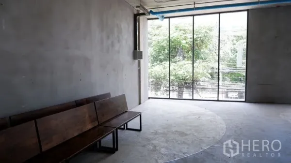 零售空间 出租在Watthana, Bangkok - 未装修转角区，整面高窗与木长椅，面向绿树与城市电线景观。