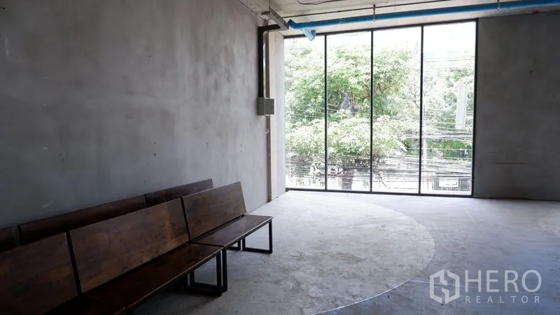 零售空间 出租在Watthana, Bangkok - 未装修转角区，整面高窗与木长椅，面向绿树与城市电线景观。