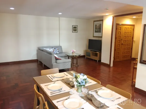 คอนโด ให้เช่าในPathum Wan, Bangkok - โถงนั่งเล่นและทานอาหารปูพื้นปาร์เกต์ โซฟาสีเทา ชั้นวางทีวี และประตูไม้ทึบ