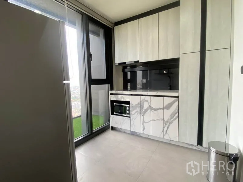 Condominium for rent in Phra Khanong, Bangkok - Modern kitchenette with marble-effect cabinetry, built-in oven and sliding glass door to the balcony.