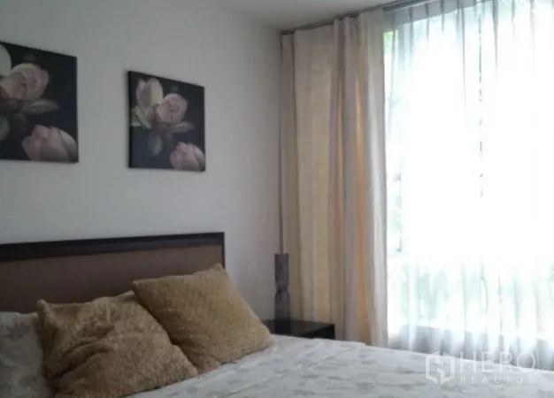 คอนโด ให้เช่าในKhlong Toei, Bangkok - ห้องนอนที่สองพร้อมหัวเตียงสีน้ำตาล รูปดอกไม้บนผนัง และหน้าต่างสูงม่านบาง