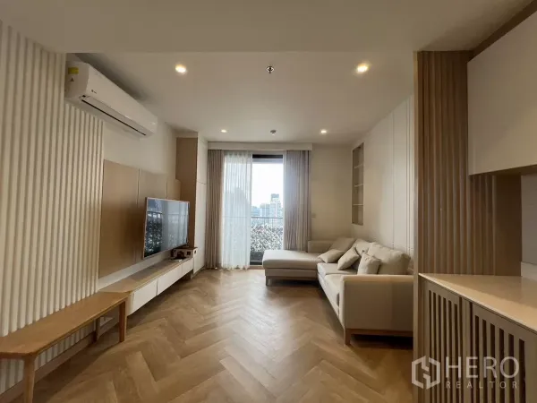 公寓 出租或出售在Chatuchak, Bangkok - 简约客厅，L形沙发、壁挂电视，通往阳台的落地门与城市景观，鱼骨拼木地板。