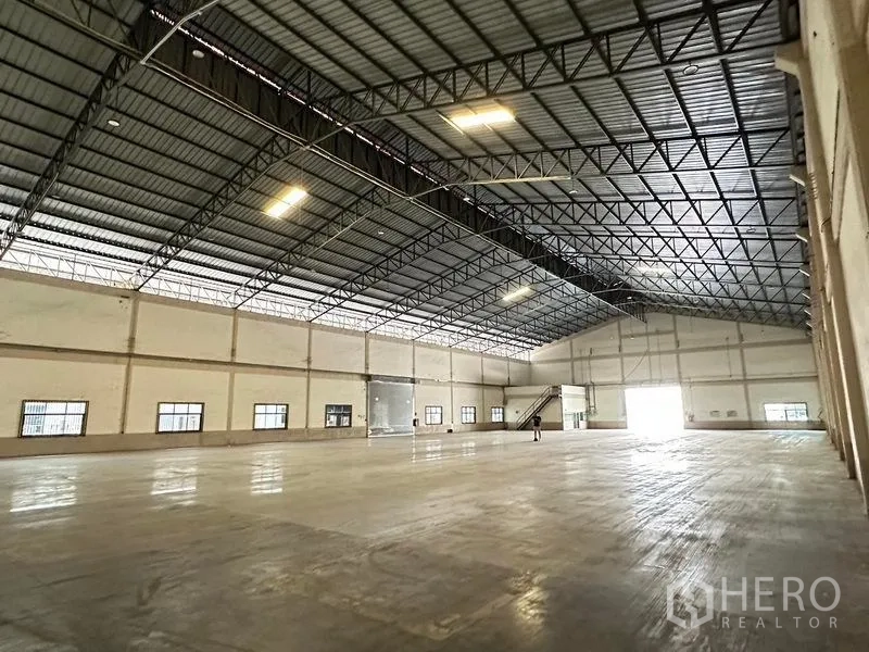 货栈 出租在Bang Sao Thong, Samut Prakan - 宽阔库内空间，采光板与钢屋架，可见通往夹层的楼梯。