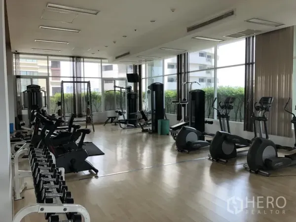 อพาร์ทเมนท์ ให้เช่าในKhlong Toei, Bangkok - ห้องฟิตเนสสว่างโปร่ง มีเครื่องคาร์ดิโอ ดัมเบล และอุปกรณ์เวท มองเห็นวิวเมืองผ่านหน้าต่างบานใหญ่