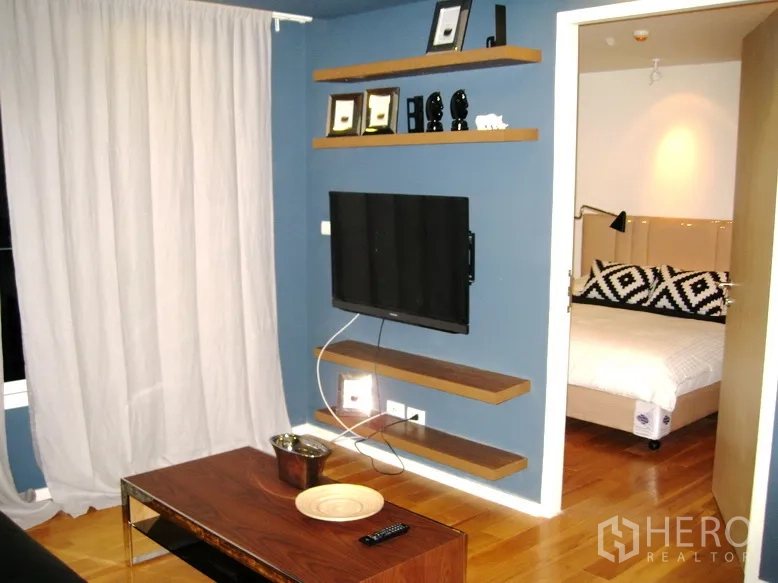 公寓 出租或出售在Bang Rak, Bangkok - 壁挂电视与悬浮层板，门口通向配几何图案靠枕的卧室。