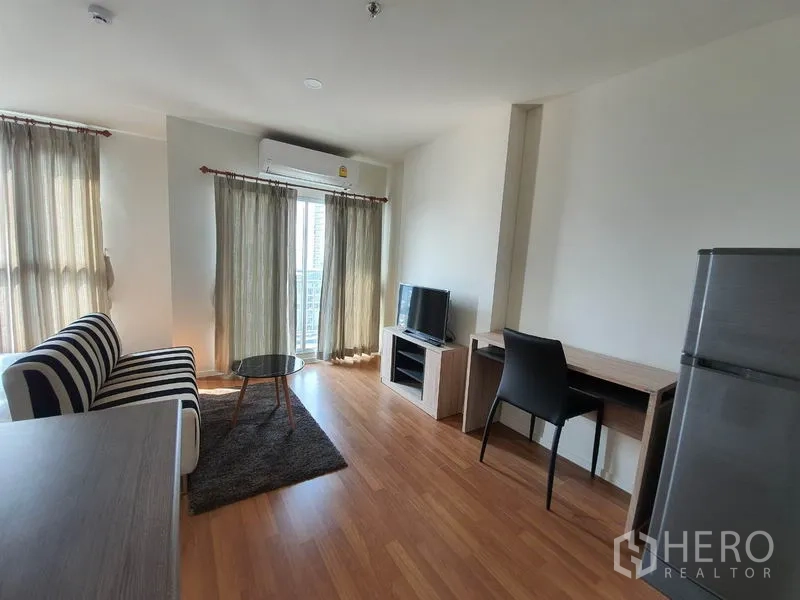 คอนโด ขายในChatuchak, Bangkok - ห้องนั่งเล่นรับแสงธรรมชาติพร้อมโซฟาลายทาง โต๊ะกลาง ทีวี และโต๊ะอ่านหนังสือใกล้ระเบียง