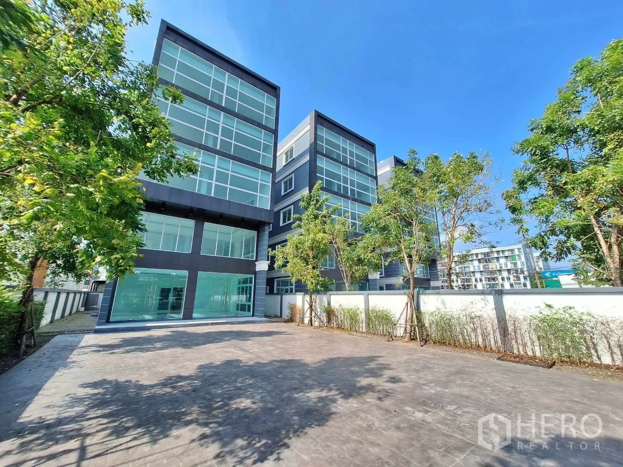 Office Space for sale in Bueng Kum, Bangkok - Side angle of contemporary office block with floor-to-ceiling windows and trees.
