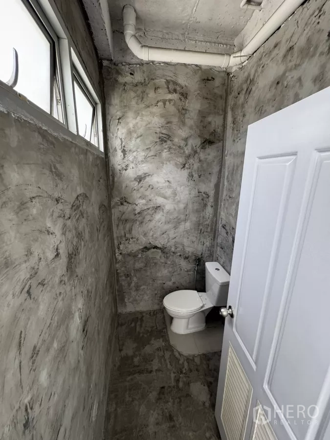 店屋 出租在Wang Thonglang, Bangkok - 混凝土质感墙面的卫生间，侧窗与白色马桶。