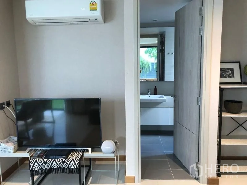 Detached House for rent or sale in Huai Khwang, Bangkok - Compact media corner with wall-mounted air conditioner and a doorway leading to a bathroom with vanity.
