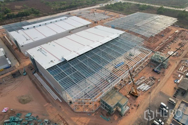 Factory for rent in Bang Bo, Samut Prakan - Aerial view of a large factory complex under construction with steel roof frames, cranes, and wide concrete access roads in an industrial estate.