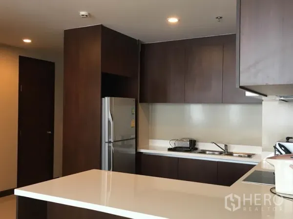 คอนโด ให้เช่าในPathum Wan, Bangkok - ครัวรูปตัว U ตู้ลายไม้เข้ม ท็อปสีขาว และตู้เย็นสแตนเลส