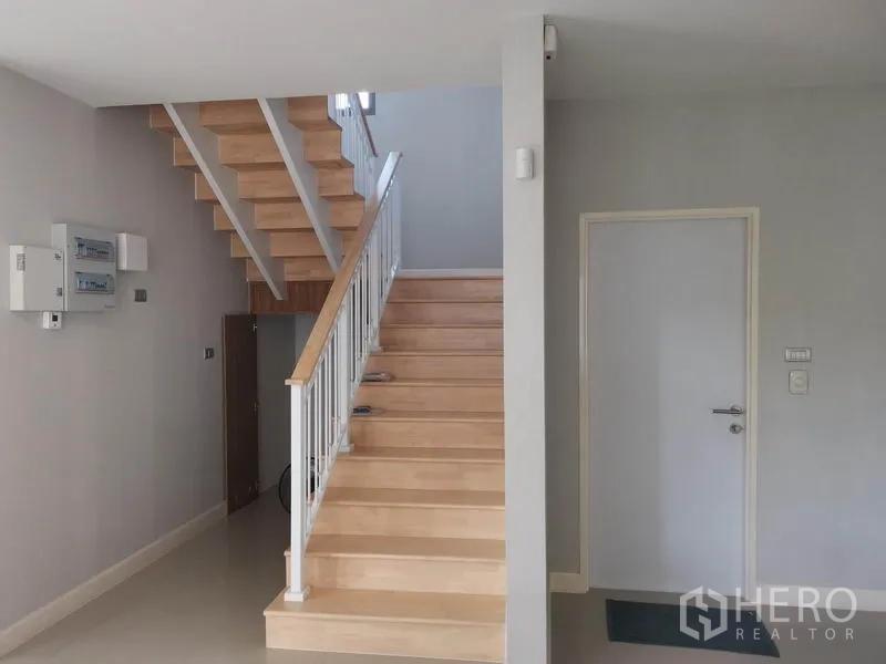 Detached House for sale in Nonthaburi - Light wood staircase with white railing and storage space under the stairs.