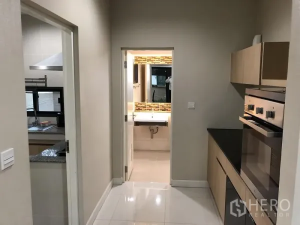 Detached House for rent in Bang Kapi, Bangkok - Hallway kitchen with built-in oven leading to a guest bathroom with mosaic backsplash.