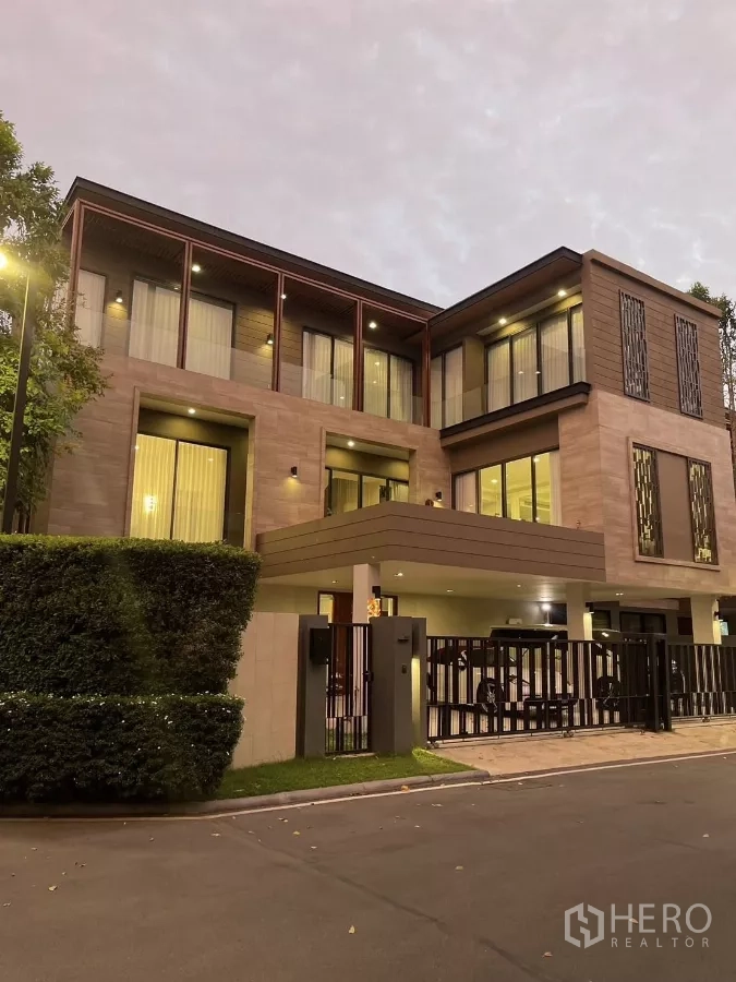 บ้าน ให้เช่าหรือขายในBang Kapi, Bangkok - มุมมองยามเย็นของบ้านหรูพร้อมไฟภายนอกและทางรถยนต์มีประตูรั้ว