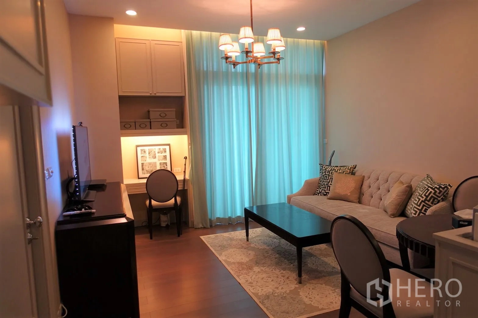 คอนโด ขายในPathum Wan, Bangkok - ห้องนั่งเล่นอบอุ่น โซฟาบุผ้า โต๊ะกลาง โคมระย้า และมุมทำงานพร้อมผ้าม่านสีฟ้า