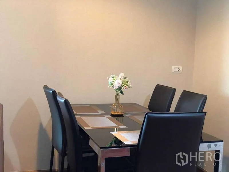 Condominium for sale in Huai Khwang, Bangkok - Close-up of four-seat dining set with flower centerpiece against a neutral wall.