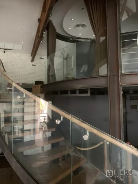 พื้นที่ขายปลีก ให้เช่าในWatthana, Bangkok - บันไดกระจกโค้งขึ้นสู่ชั้นลอย พร้อมไฟสปอตไลต์และงานตกแต่งสมัยใหม่