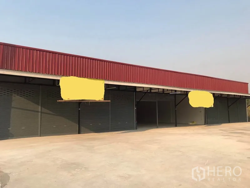 คลังสินค้า ให้เช่าในLam Luk Ka, Pathum Thani - ด้านหน้าอาคารโกดังชั้นเดียว แผงกันสาดสีแดง พร้อมประตูม้วนหลายช่อง.