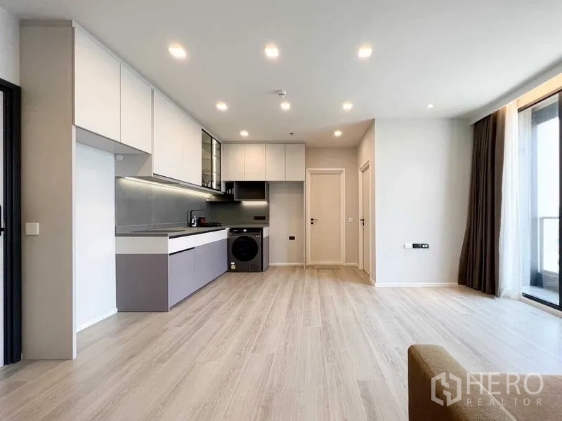 Condominium for rent or sale - Open-plan kitchen and living space with light wood flooring and balcony doors.