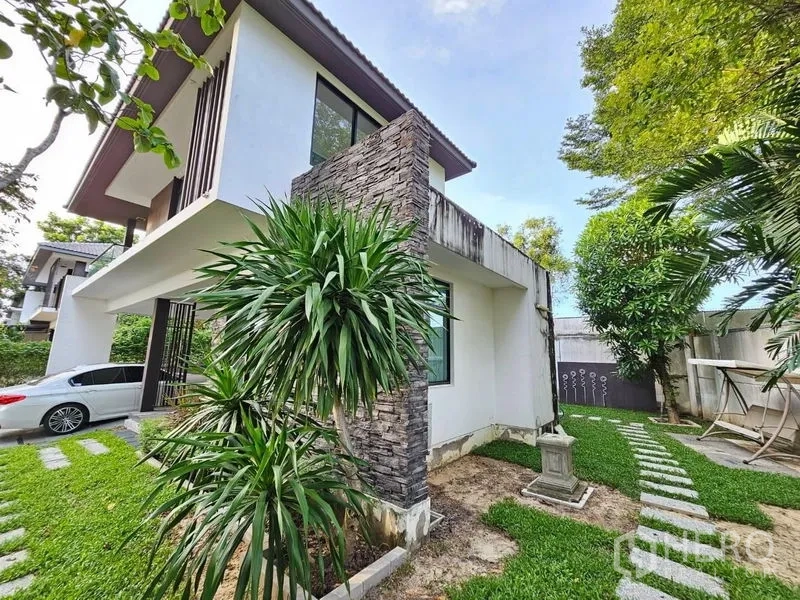 Detached House for sale in Prawet, Bangkok - Side garden with stone feature wall, mature plants and stepping‑stone walkway.